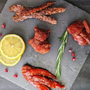 Delicious smoked salmon varieties including salmon strips, chunks, and slices on a slate serving boa.