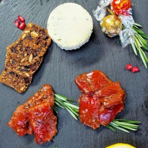 Assorted smoked salmon with cheese, crackers, chocolates, and garnishes on slate.
